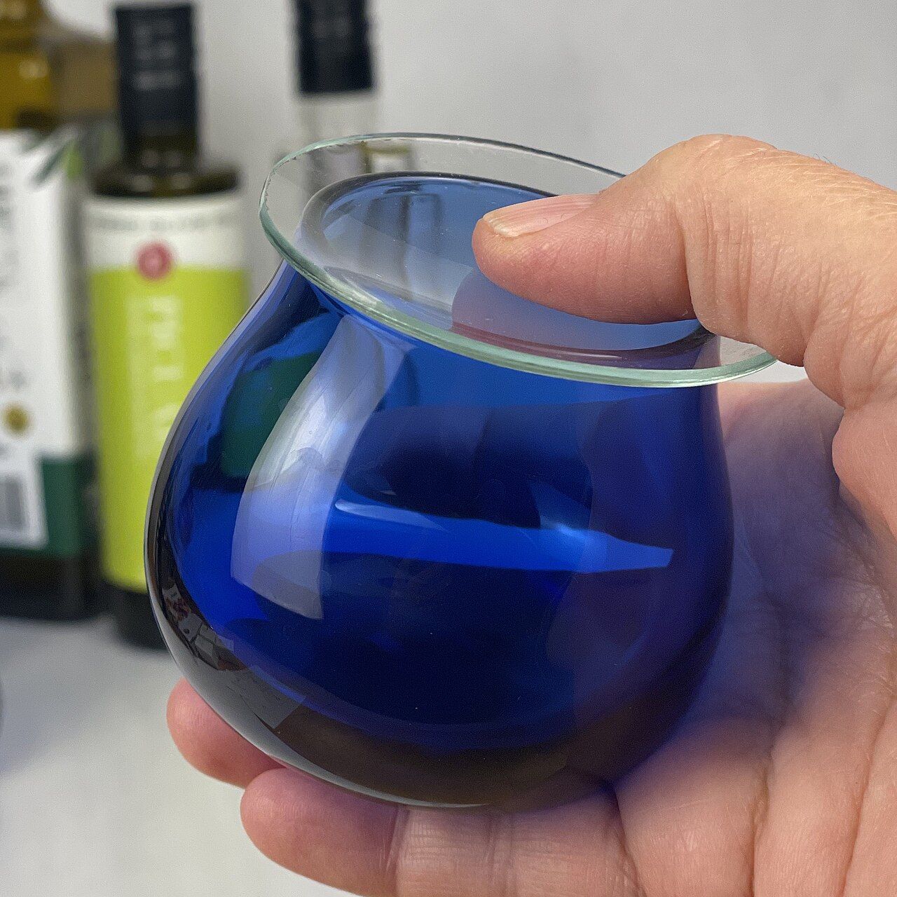 Verre de dégustation d'huile d'olive en verre bleu cobalt, recouvert d'un verre de montre, tenu dans la main